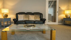 A living room with a glass coffee table, black leather sofa, and two lamps on side tables.