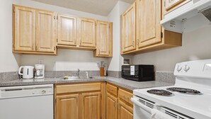 A kitchen with wooden cabinets, a white dishwasher, a white stove, and a black microwave.