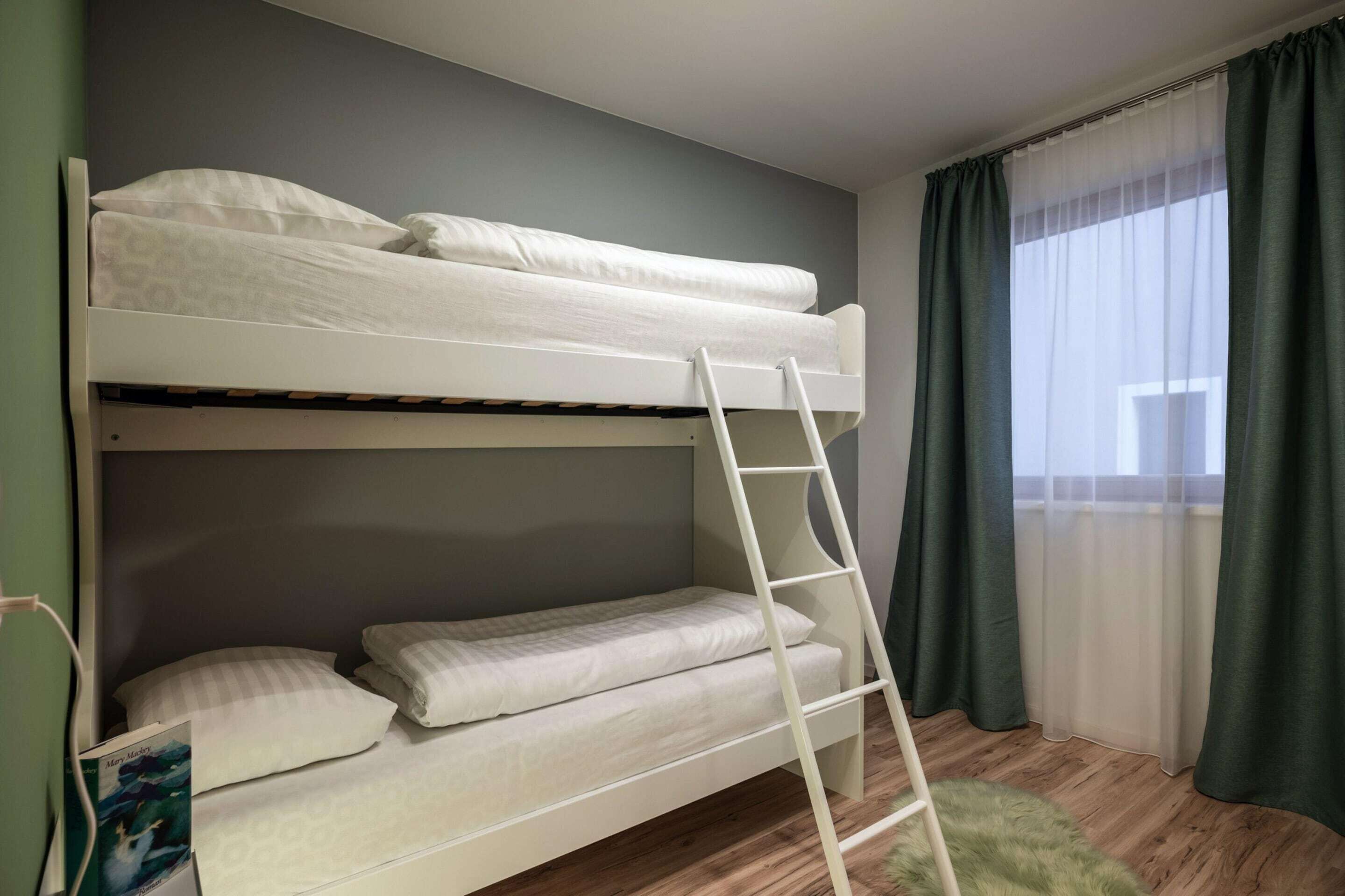 Un lit superposé avec une échelle, un rideau vert et une fenêtre.