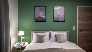 Une chambre d’hôtel avec un lit, une table de chevet, une lampe, deux tableaux encadrés au mur et une porte en bois.