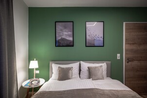 Una habitación de hotel con una cama, una mesita de noche, una lámpara, dos cuadros en la pared y una puerta de madera.
