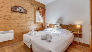 A cozy bedroom with wooden walls, a bed with white linens, a teddy bear on the bed, and a window with curtains.