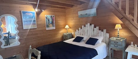Une chambre confortable, aménagée dans un chalet en bois, avec un lit, deux tables de chevet, une chaise et une petite table.