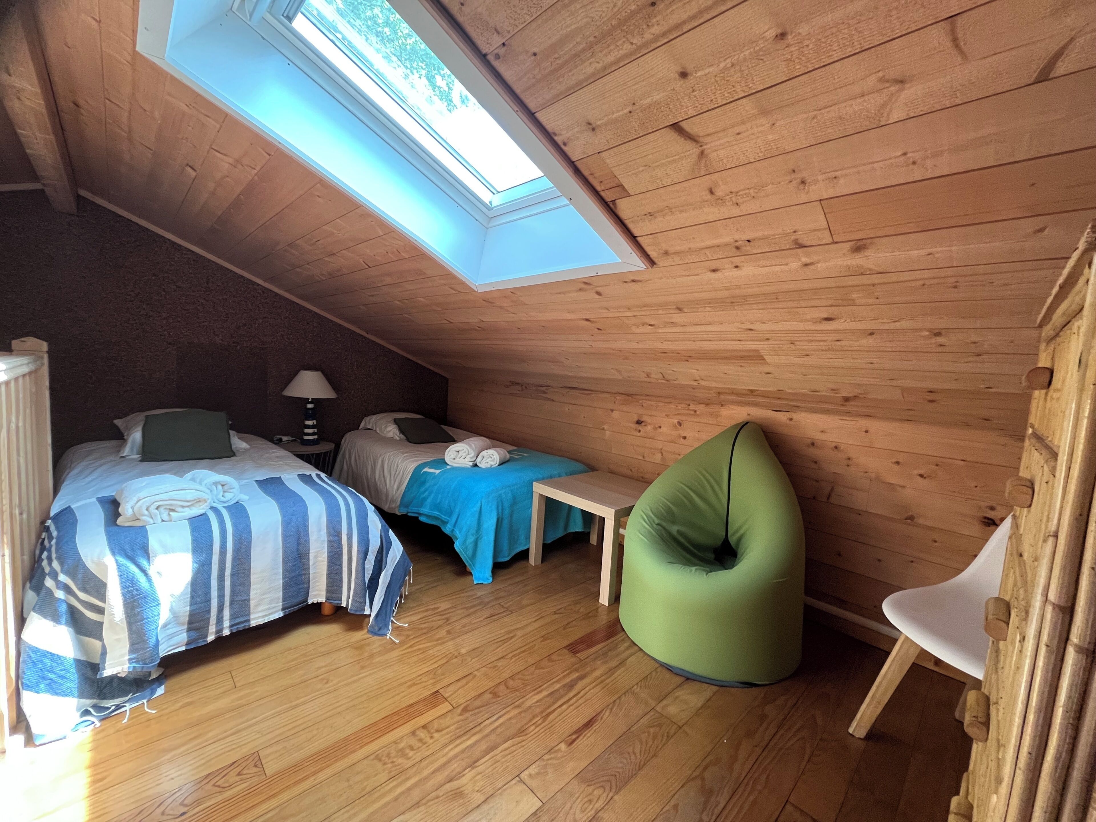 A room with two beds, a green bean bag chair, a small table, and a skylight.