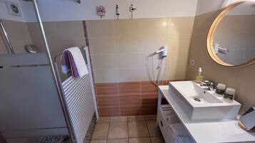 A bathroom with a shower, a sink with toiletries, and a mirror.