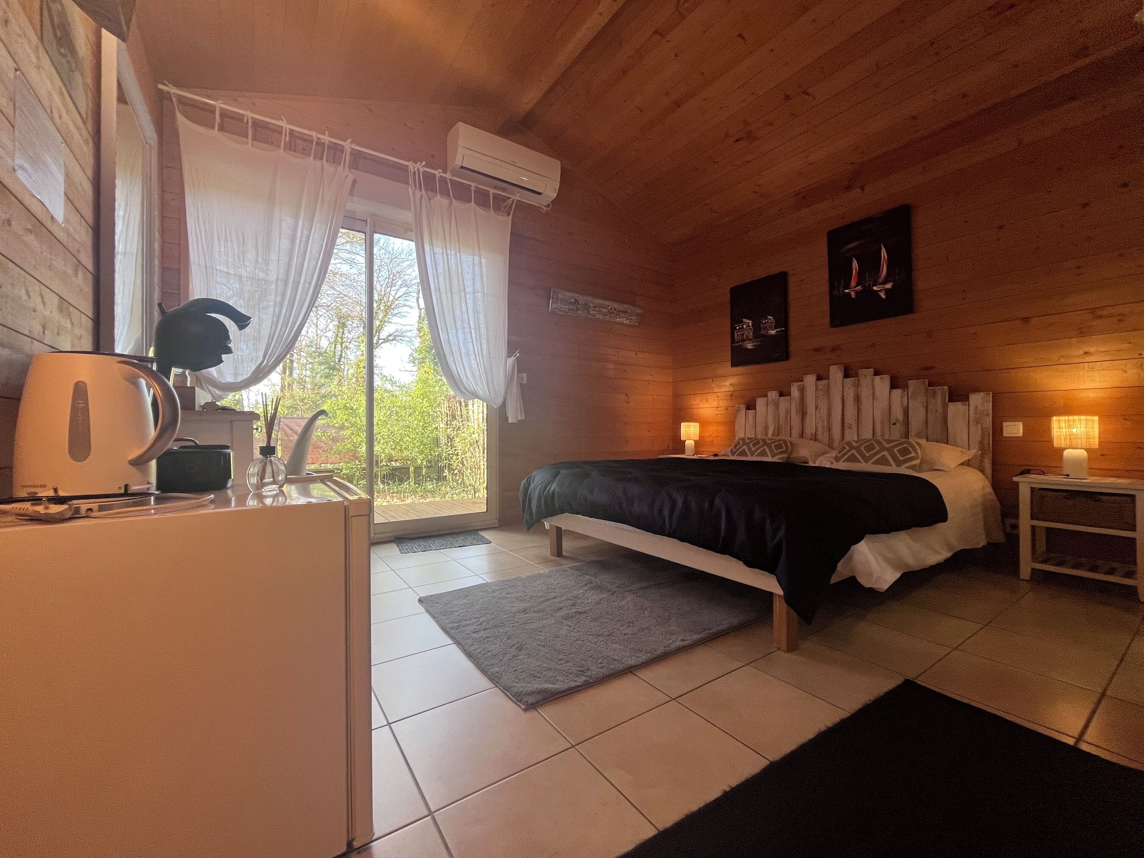 Een gezellig houten slaapkamer met een bed, bedlampjes, een koffiezetapparaat en uitzicht op de natuur.