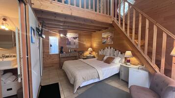 Un dormitorio acogedor con una escalera de madera, una cama con almohadas, una mesita de noche, una silla y un baño con lavabo y espejo.