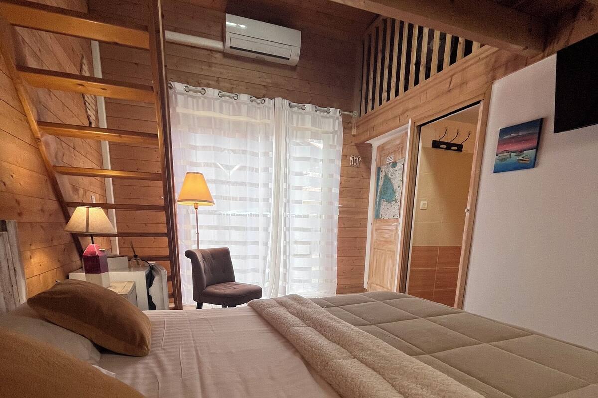Une chambre à coucher avec un lit, une chaise, un bureau, une lampe et une fenêtre avec des rideaux.