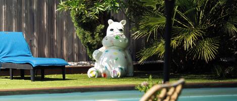 A pool area with a white statue of a cow, a blue lounge chair, and a wooden fence in the background.