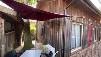 Una cabaña de madera con una mesa y sillas bajo un paraguas rojo, una ventana y una puerta.
