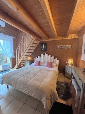 A bedroom with a bed, a wooden staircase, a small desk, and a wall-mounted picture. - VILLA HERBERT (Andernos-les-Bains)