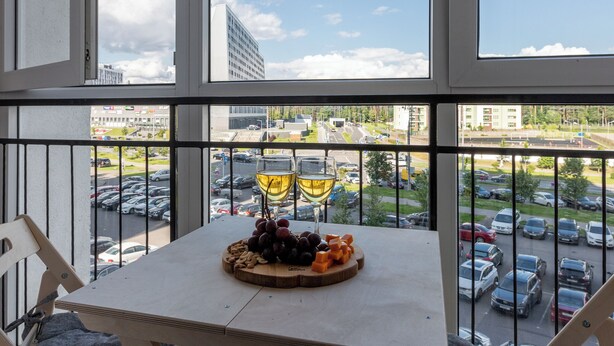 Un balcon avec une table dressée pour deux personnes, une vue sur un parking et un ciel dégagé.