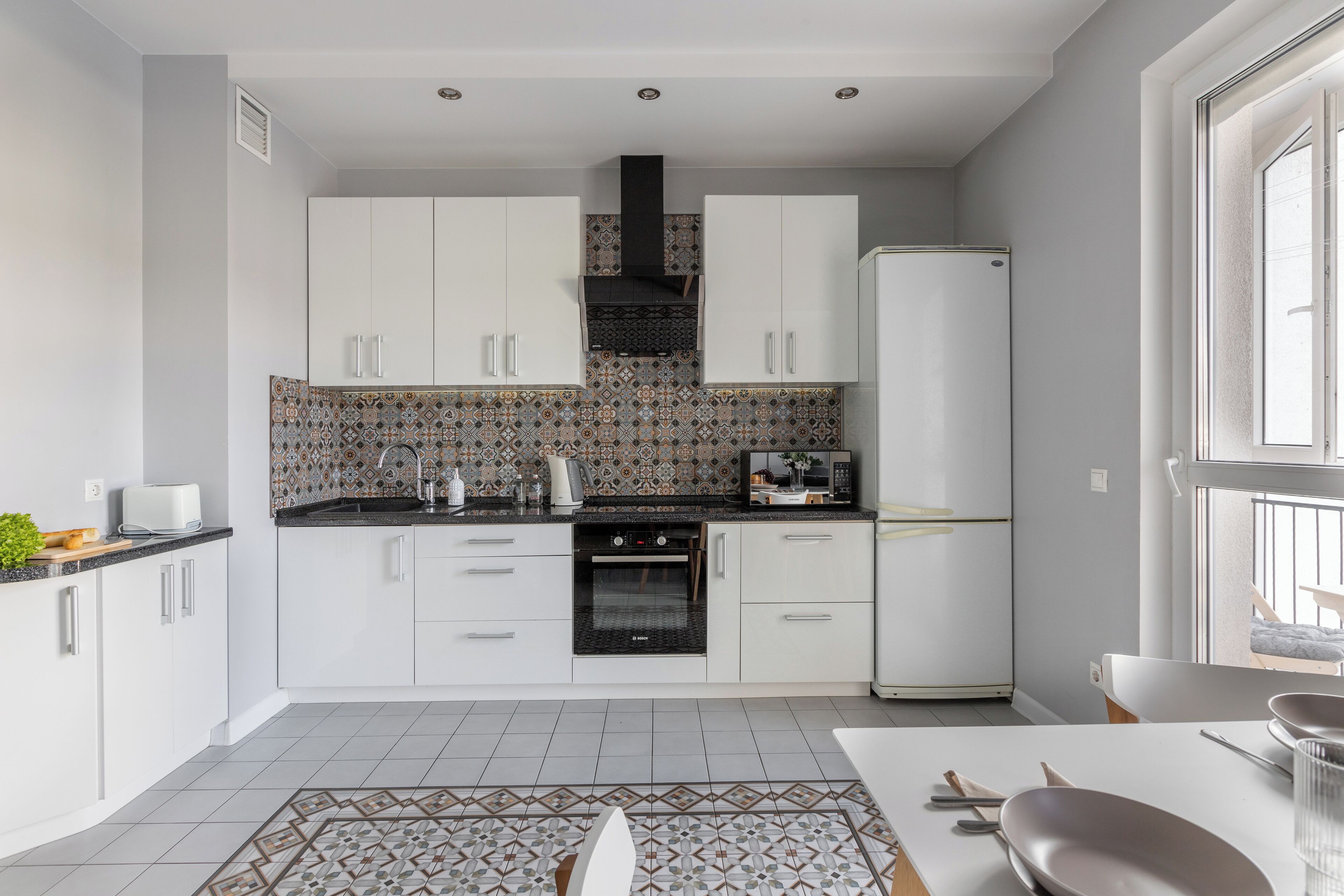 Een moderne keuken met witte kastjes, een decoratieve spatwand en een ingebouwde oven.