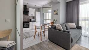 Un salon moderne avec un canapé gris, une table à manger avec des chaises, et une cuisine en arrière-plan.