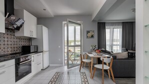 Une cuisine moderne avec des armoires blanches, un four à micro-ondes et un pare-feu décoratif. On y trouve un coin repas avec une table et des chaises, ainsi qu’un canapé dans le salon.