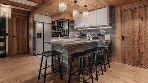 Une cuisine moderne avec des poutres en bois, un îlot en marbre, des tabourets de bar et des luminaires suspendus.