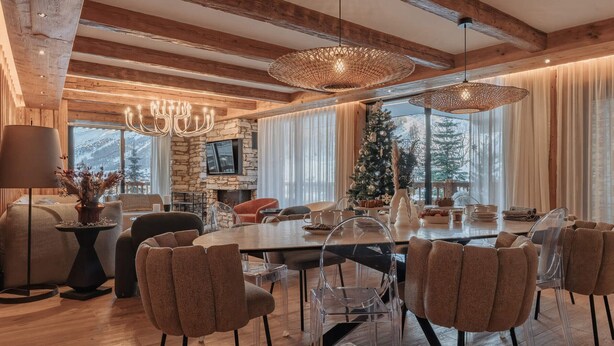 Un espace repas moderne avec une grande table en bois, des chaises transparentes et une cheminée en pierre.