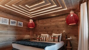 Une pièce chaleureuse aux murs en bois, avec un lit, une lampe suspendue rouge et une petite table de chevet.