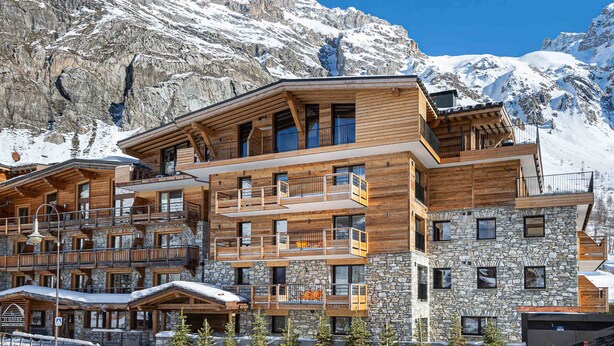 A multi-story wooden building with balconies, stone accents, and a mountainous backdrop. - Charming stay at Val-d'Isère for 4 guests with ski-in/ski-out (Val-d'Isère)