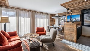 A modern living room with a sofa, armchair, and coffee table. There is a dining area with a table and chairs, and a kitchen area with a wooden counter and a large window. - Charming stay at Val-d'Isère for 4 guests with ski-in/ski-out (Val-d'Isère)