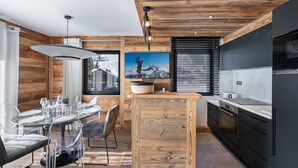 A modern kitchen with wooden accents, a dining area with clear chairs, and a large island. - Charming stay at Val-d'Isère for 4 guests with ski-in/ski-out (Val-d'Isère)