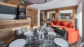 A modern interior with a dining area set for six, a kitchen with wooden accents, and a living area with a sofa and red cushions. - Charming stay at Val-d'Isère for 4 guests with ski-in/ski-out (Val-d'Isère)