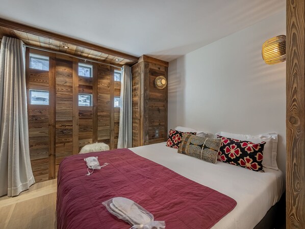A hotel room with a wooden wall panel design, a bed with a red quilt, and a small white fluffy stool. - Modern apartment in Val d'Isère, 6 people, direct ski area access (Val-d'Isère)