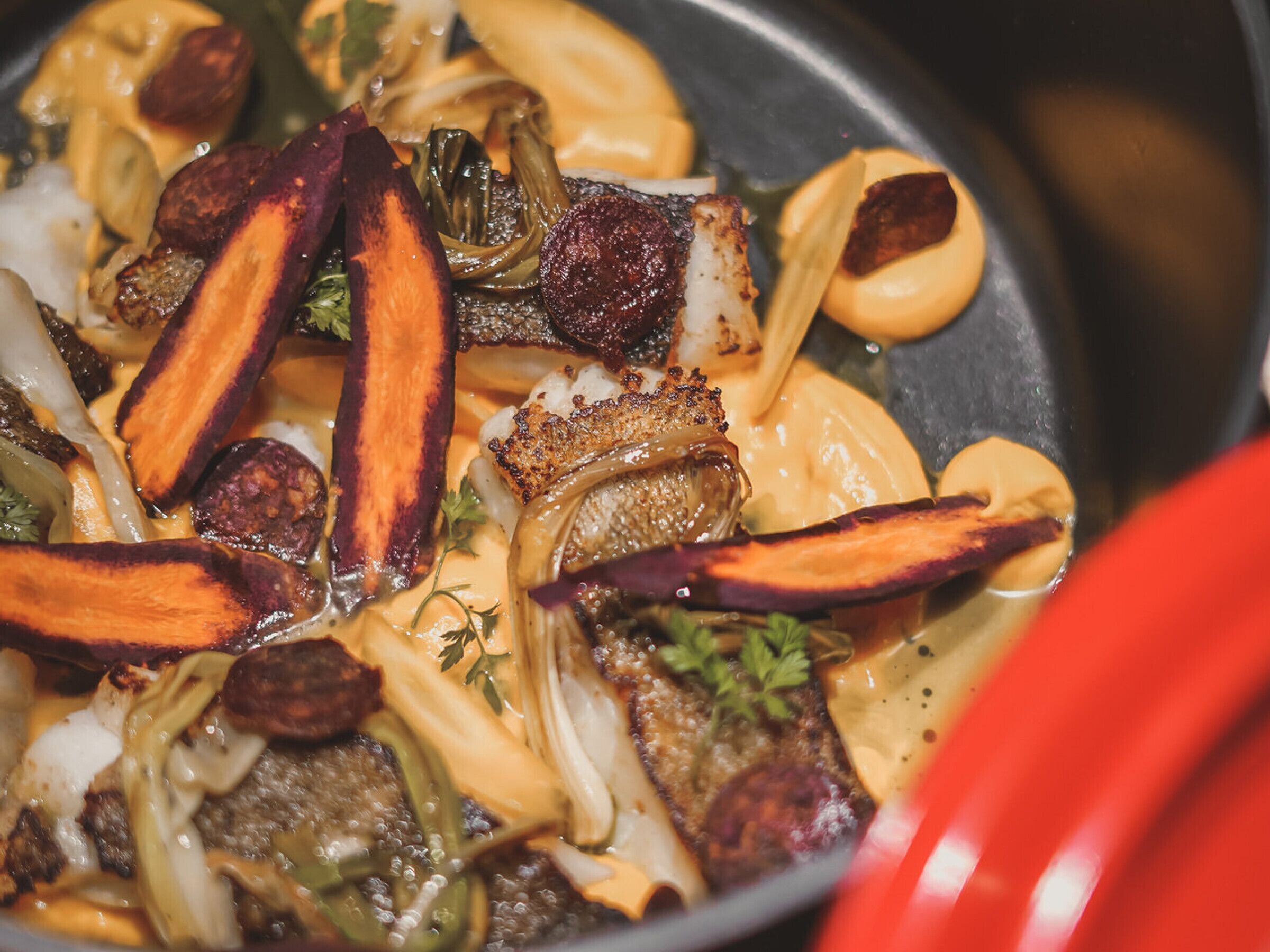 Un primo piano di un piatto con diversi ingredienti, tra cui sembra esserci carne, verdure e forse formaggio, in una padella.