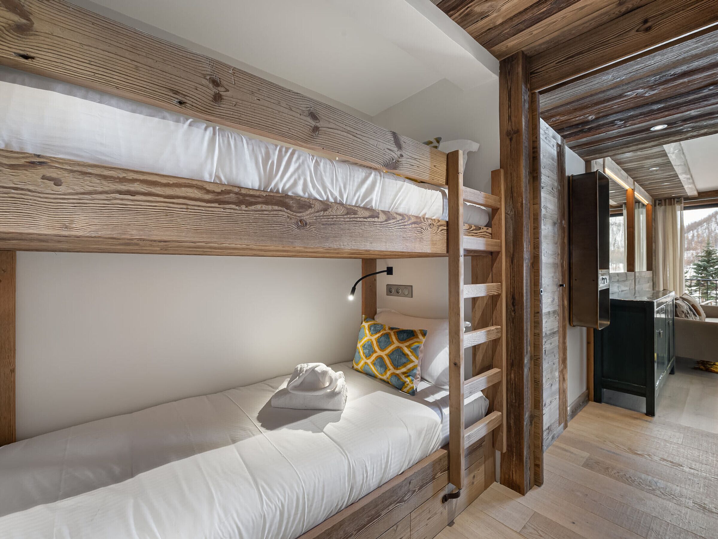 Un lit superposé avec une literie blanche, une tête de lit en bois et une petite table de chevet avec une lampe.