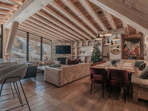 A cozy interior with a stone fireplace, wooden beams, a dining area, and a Christmas tree.