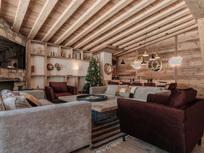 A rustic interior with exposed wooden beams, a fireplace, a Christmas tree, and a cozy seating area.