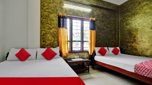 Habitación de hotel con dos camas, ropa de cama roja y blanca, una ventana con cortinas y una mesita con una botella y vasos.