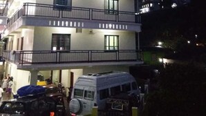 Un edificio de dos pisos con balcones y un vehículo estacionado al frente.