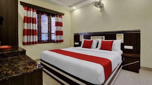 Habitación de hotel con una cama grande, cabecera de madera, encimera de mármol y una ventana con cortinas rojas y blancas.