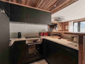 A modern kitchen with dark cabinets, a Bosch oven, a built-in stove, and wooden ceiling beams.