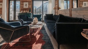 Una sala de estar acogedora con sofá, sillones y una mesa de centro, con vistas a la montaña a través de amplios ventanales.