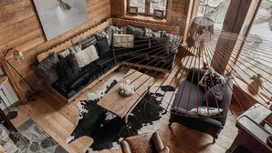 A cozy cabin interior with a wooden floor, a black sofa, a cowhide rug, and a rustic wooden table.