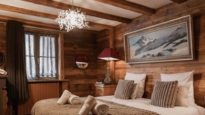A cozy wooden room with a large bed, a painting of mountains, and a unique chandelier.