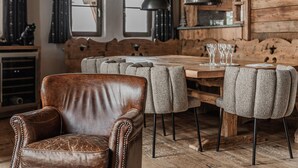 A rustic dining area with a wooden table, upholstered chairs, and a leather armchair.