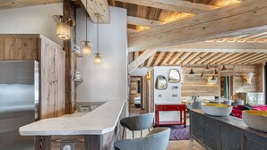 A modern kitchen with wooden beams, a stainless steel refrigerator, and a bar area with stools.