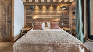 A bedroom with a wooden ceiling, two bedside tables, a bed with patterned bedding, and wall-mounted lamps.