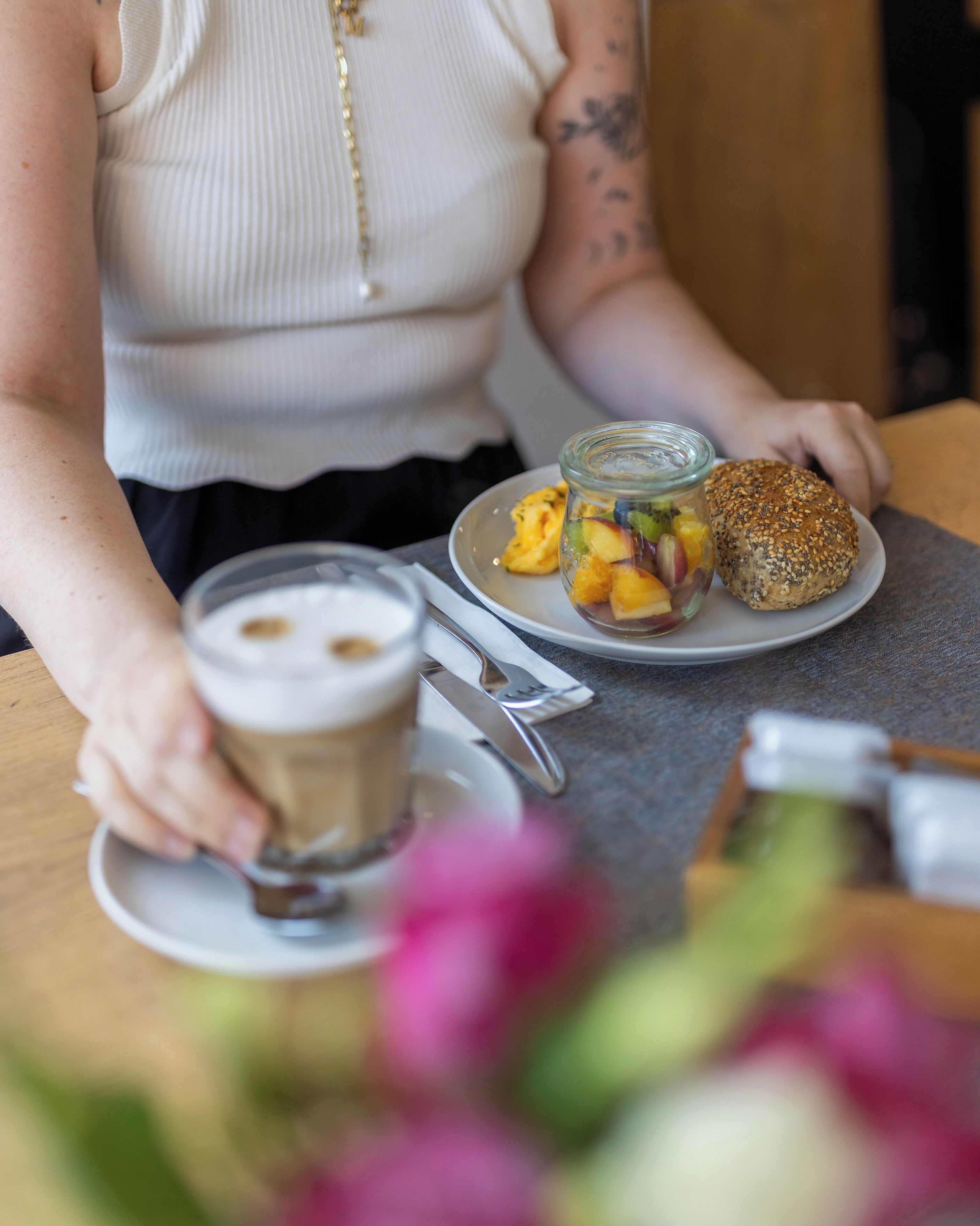 A person holding a cup of coffee and a plate with a sandwich and a jar of fruit salad.