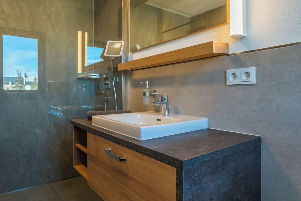 Een moderne badkamer met een grote spiegel, een ingebouwd wastafeltje en een houten wastafelmeubel.