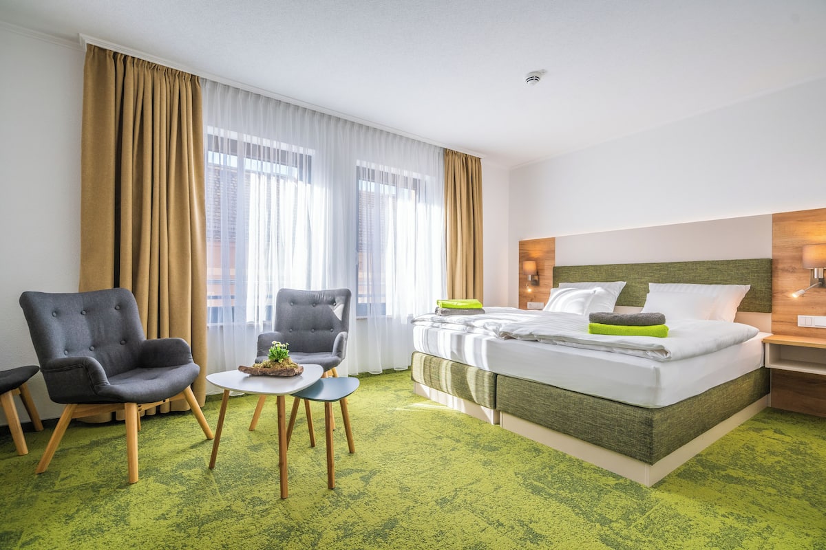 Een hotelkamer met een bed, twee fauteuils, een klein tafeltje en een groen tapijt.