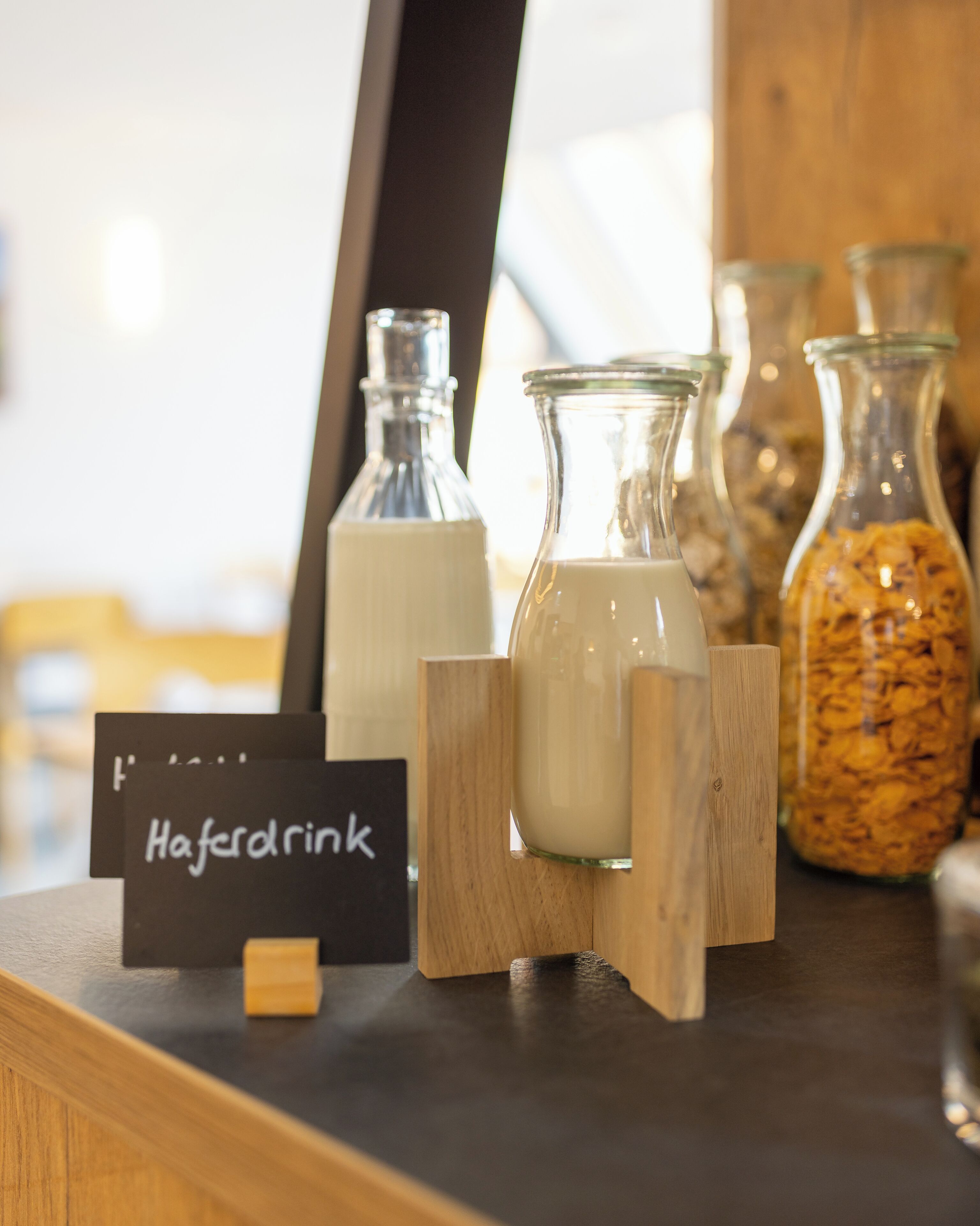 A display of milk bottles and a jar of cereal on a wooden counter with a sign reading "Haferdrink".