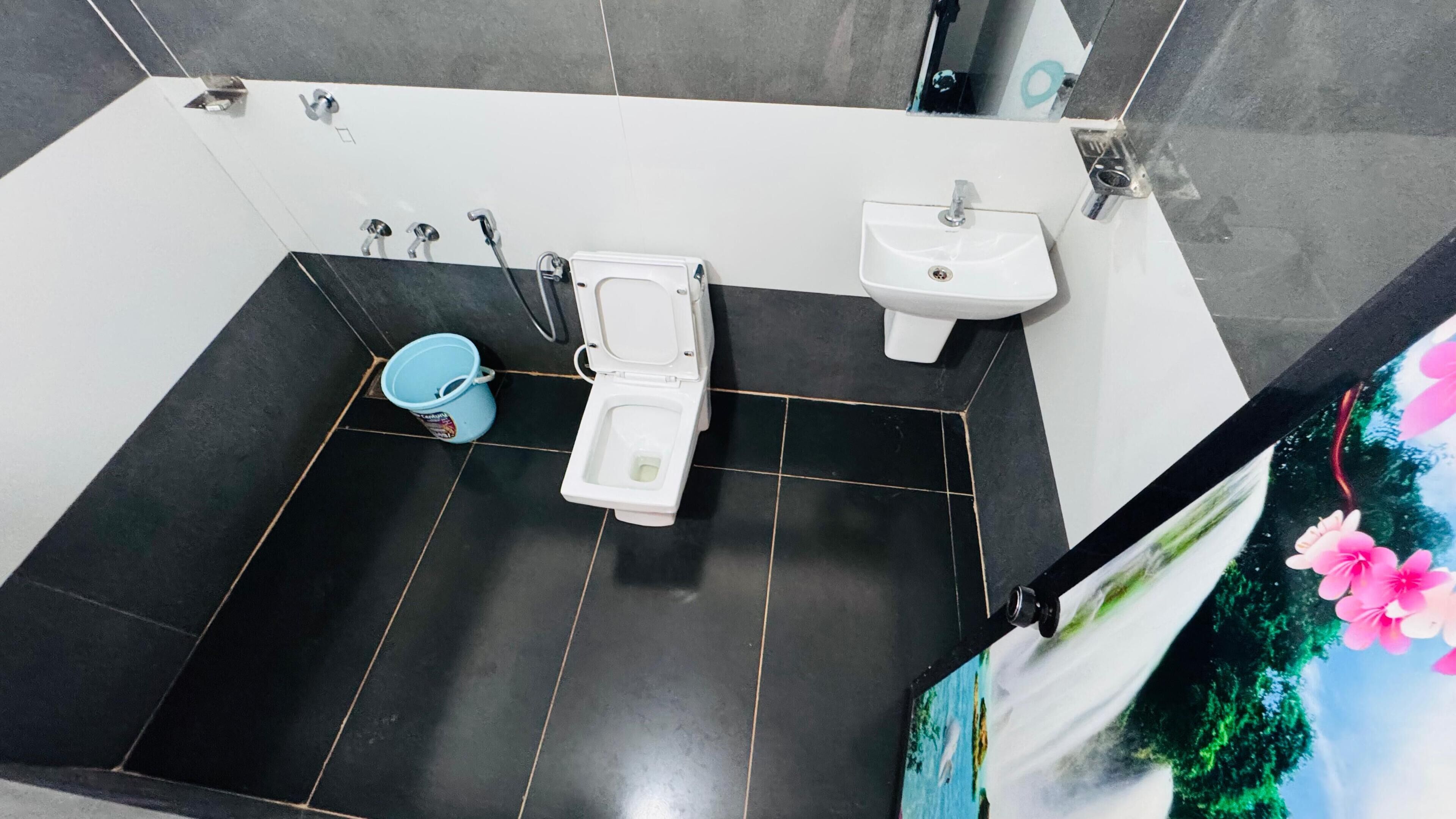 A bathroom with a toilet, bidet, and sink, tiled floor, and a bucket.