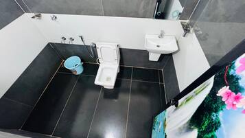 A bathroom with a toilet, bidet, and sink, tiled floor, and a bucket.