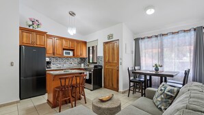 A compact kitchen with wooden cabinets, a black refrigerator, and a microwave. There's a dining area with a table and chairs, and a sofa in the living room. - Green Turtle 20 in Coco is an elegantly appointed 2-bedroom, 1-bath condo with a swimming pool located within a 7-minute walk of the beach. <br><br>📢Important announcement: Golf cart with condo available upon request for additional charges (Playas Del Coco)