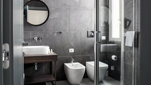 Ein modernes Badezimmer mit Duschkabine aus Glas, einem runden Spiegel, einem weißen Waschbecken und einem Bidet.