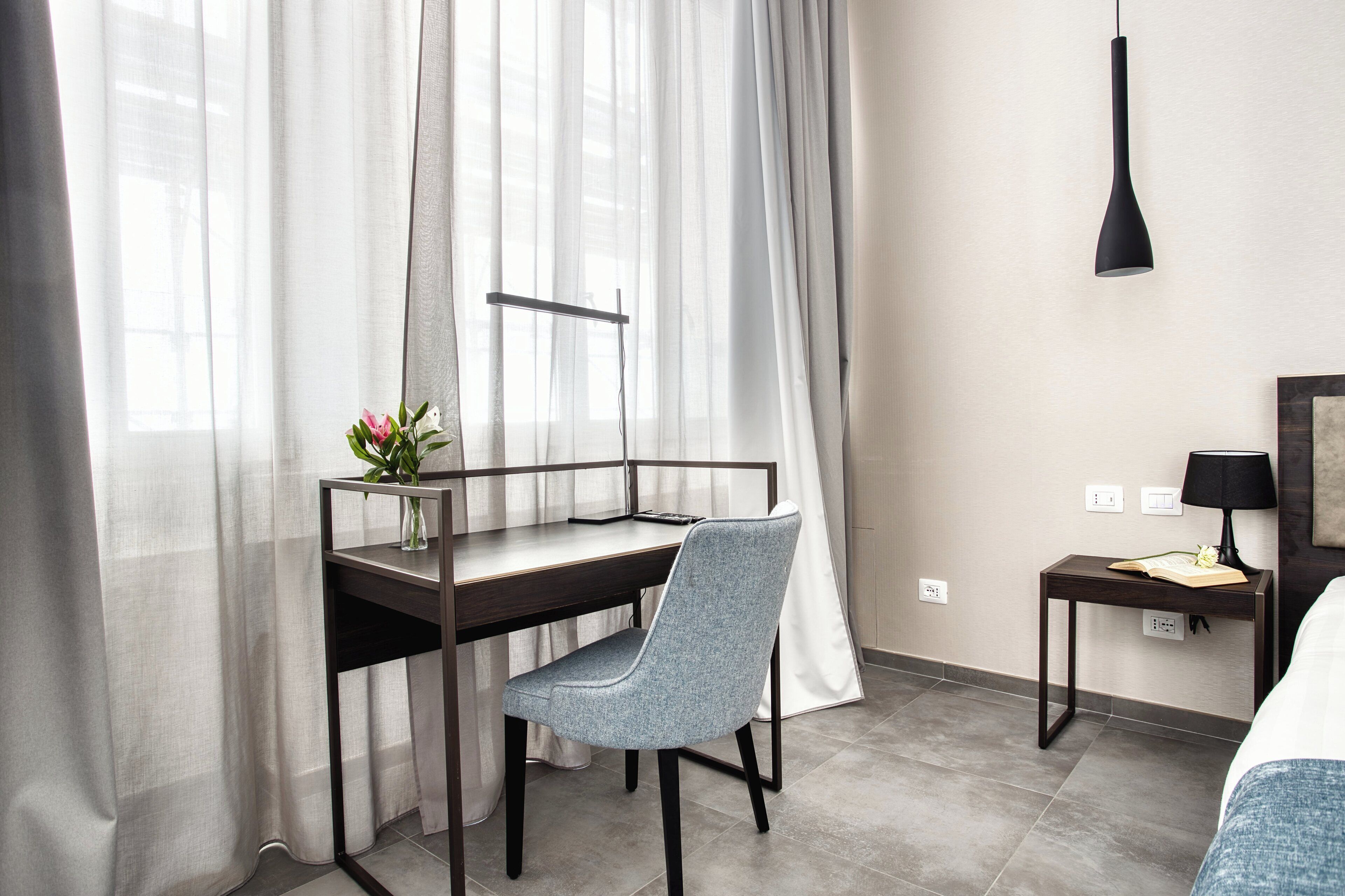 Ett modernt hotellrum med ett skrivbord, en stol och ett nattduksbord med en lampa.